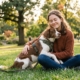 Frau sitzt entspannt mit ihrem Hund im Y-Geschirr im Park
